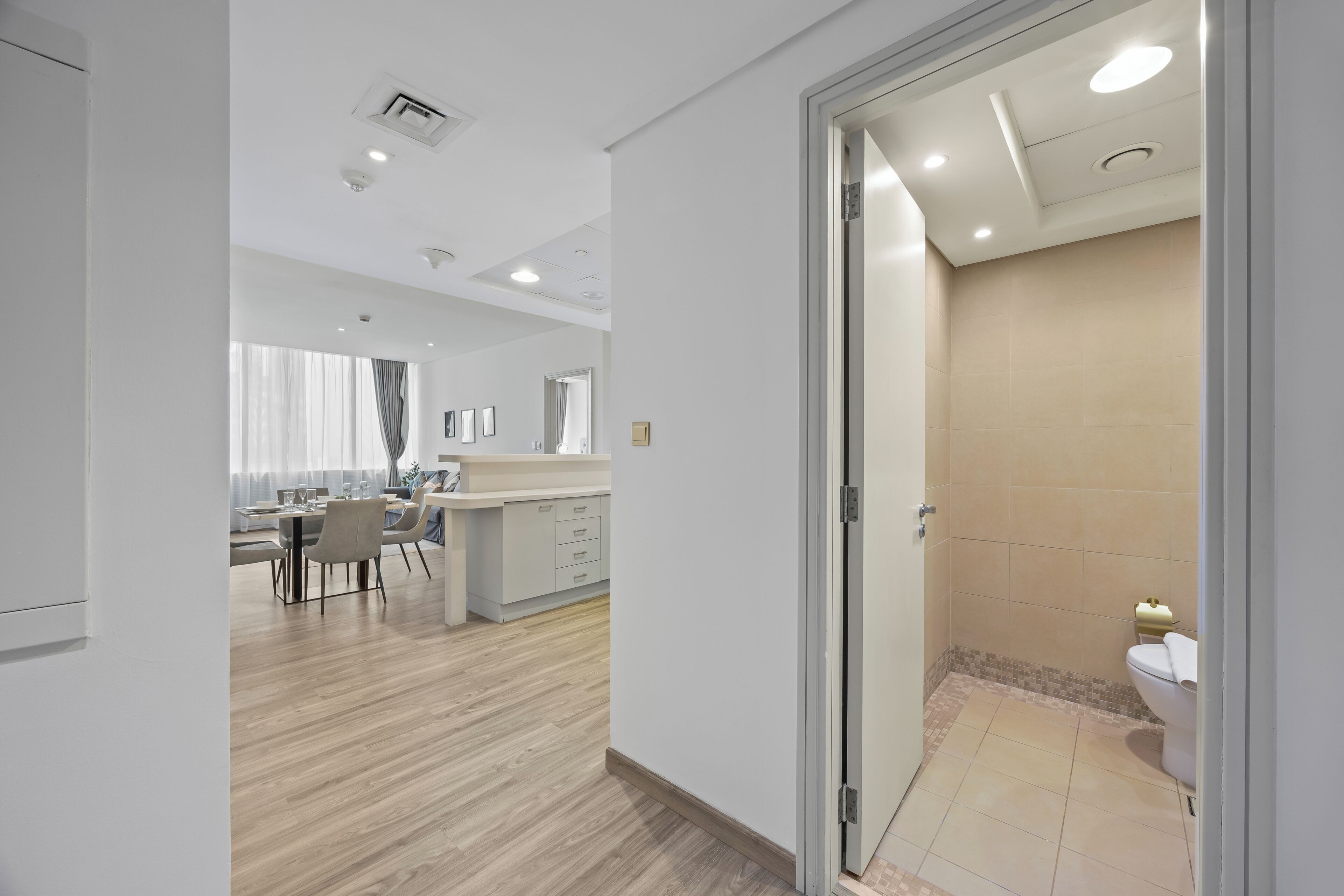 A modern hotel room with a wooden floor, a bathroom with a toilet and shower, and a dining area with a table and chairs.