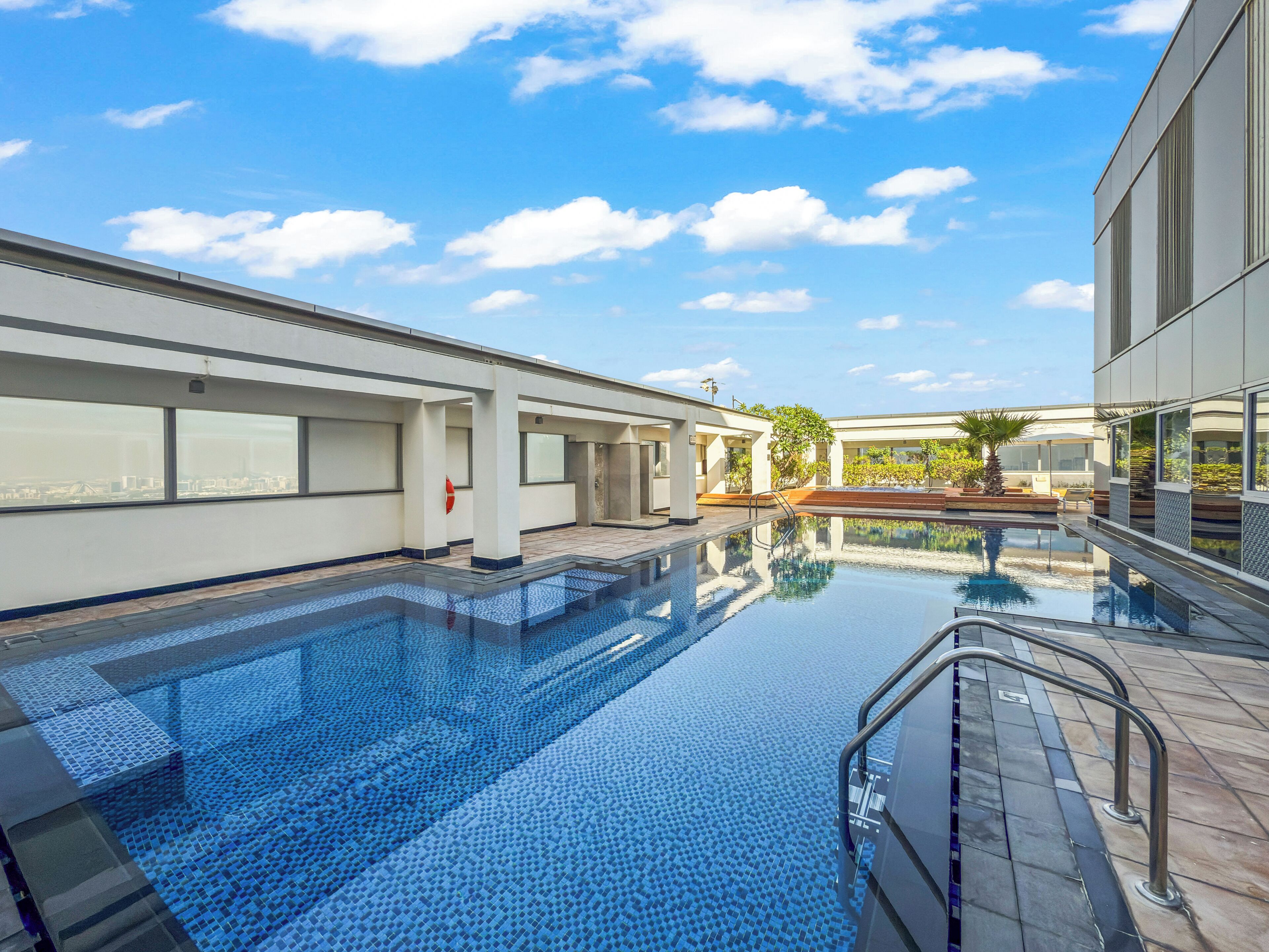 A modern hotel with a large outdoor swimming pool, a covered seating area, and a view of the city skyline.