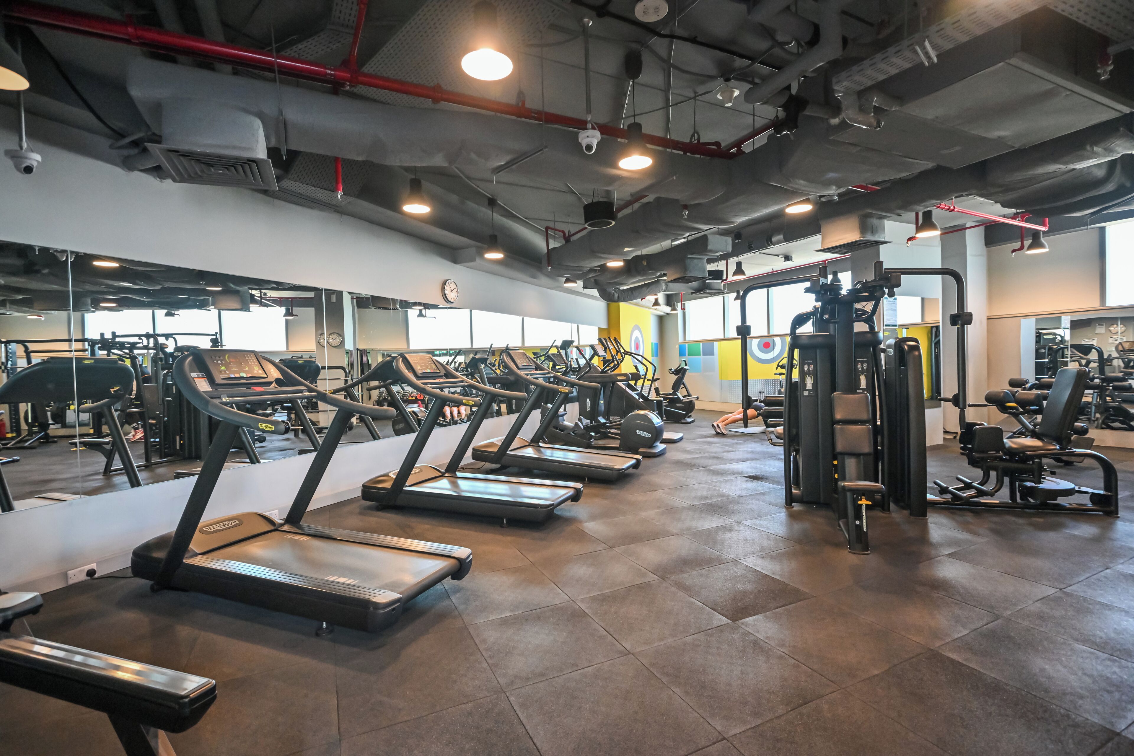 Un gimnasio con cintas de correr, máquinas de pesas y un espejo grande.