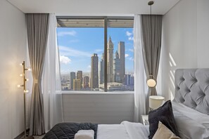 Une chambre d’hôtel avec une grande fenêtre, un lit avec une literie blanche et noire, une lampe de chevet et une vue sur le paysage urbain.