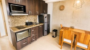 Una cocina compacta con armarios de madera oscura, electrodomésticos de acero inoxidable, encimera de granito y una mesa de comedor de madera.