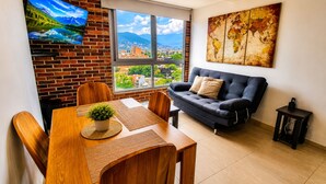 Un comedor con pared de ladrillo, un televisor montado en ella, una mesa de madera con sillas, un sofá y un mapa mundial en la pared.