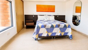 Un dormitorio con cama, mesita de noche, cajón, espejo y ventana.