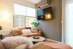 A modern living room with a sofa, a round coffee table, and a flat-screen TV mounted on a wooden wall.