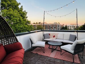 A rooftop terrace with a sofa set, a small round table, and string lights.
