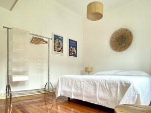 A bedroom with a bed, a hanging rack, a lamp, and two posters on the wall.