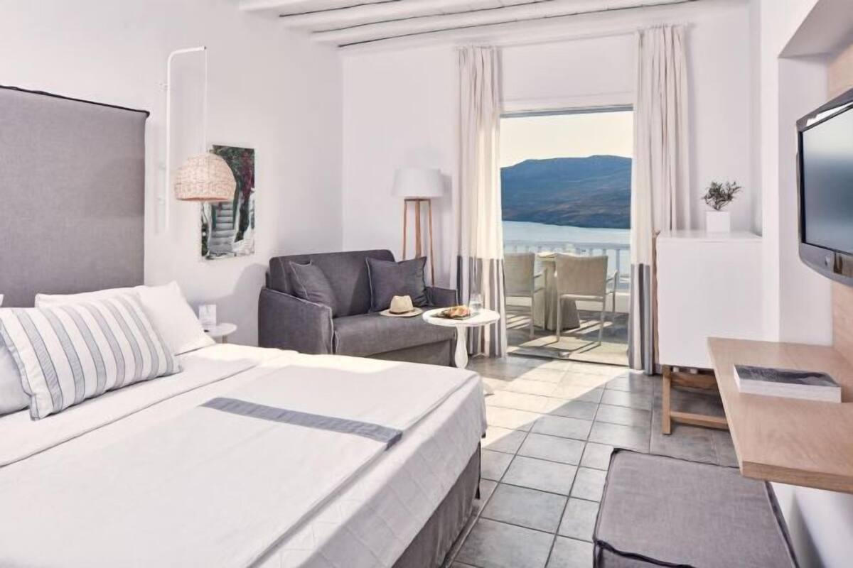 Une chambre d’hôtel avec un lit, un canapé, une petite table, une télévision et un balcon avec vue.