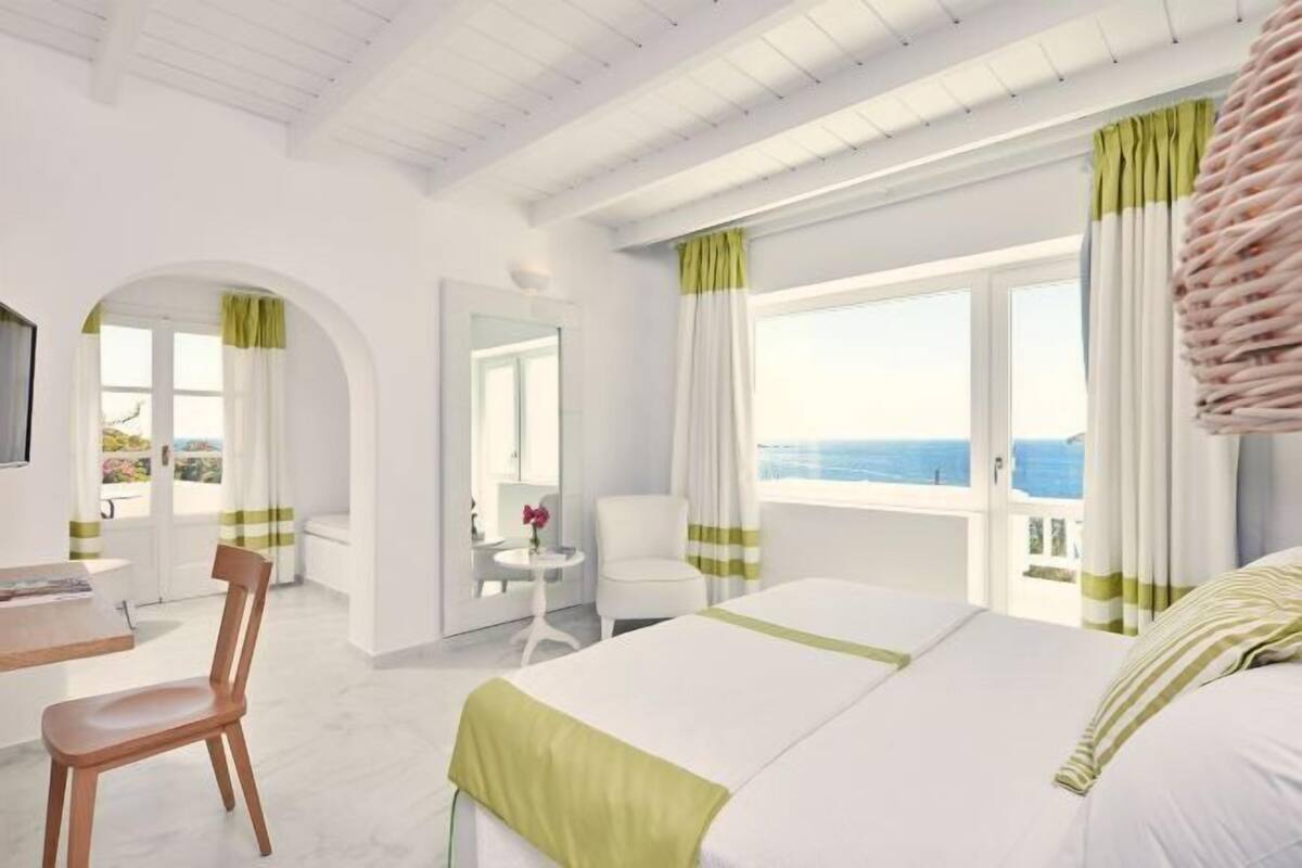 Une chambre d’hôtel avec un lit, un bureau, une chaise et une vue sur la mer.
