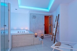 A modern bathroom with a glass shower enclosure, a freestanding bathtub, and a wooden door leading to another room.