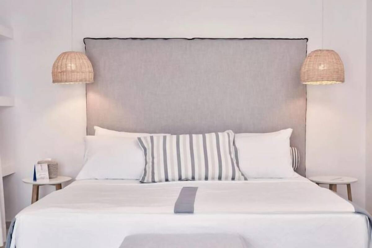 Une chambre d’hôtel avec un grand lit, deux tables de chevet et deux lampes fixées au mur.