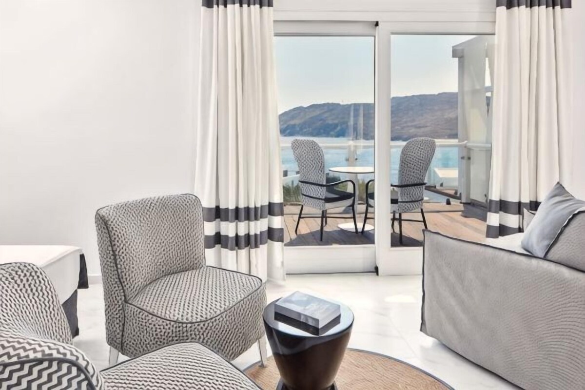 A modern living room with patterned furniture, a coffee table, and a view of a balcony with outdoor seating.