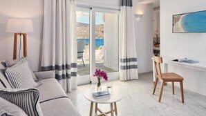 Une chambre d’hôtel moderne avec un canapé, une petite table sur laquelle sont posés un livre et des fleurs, un fauteuil et une vue sur la mer par de grandes fenêtres.