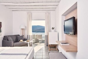 Hotelkamer met een bed, een bank, een televisie, een klein tafeltje en een balkon met uitzicht op zee.