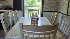 Un comedor con una mesa larga y seis sillas, un ventilador de techo y vistas a zonas verdes.