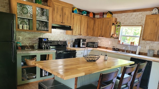 Una cocina con armarios de madera, encimera de granito, estufa integrada, un lavamanos y una ventana con vista a la vegetación.