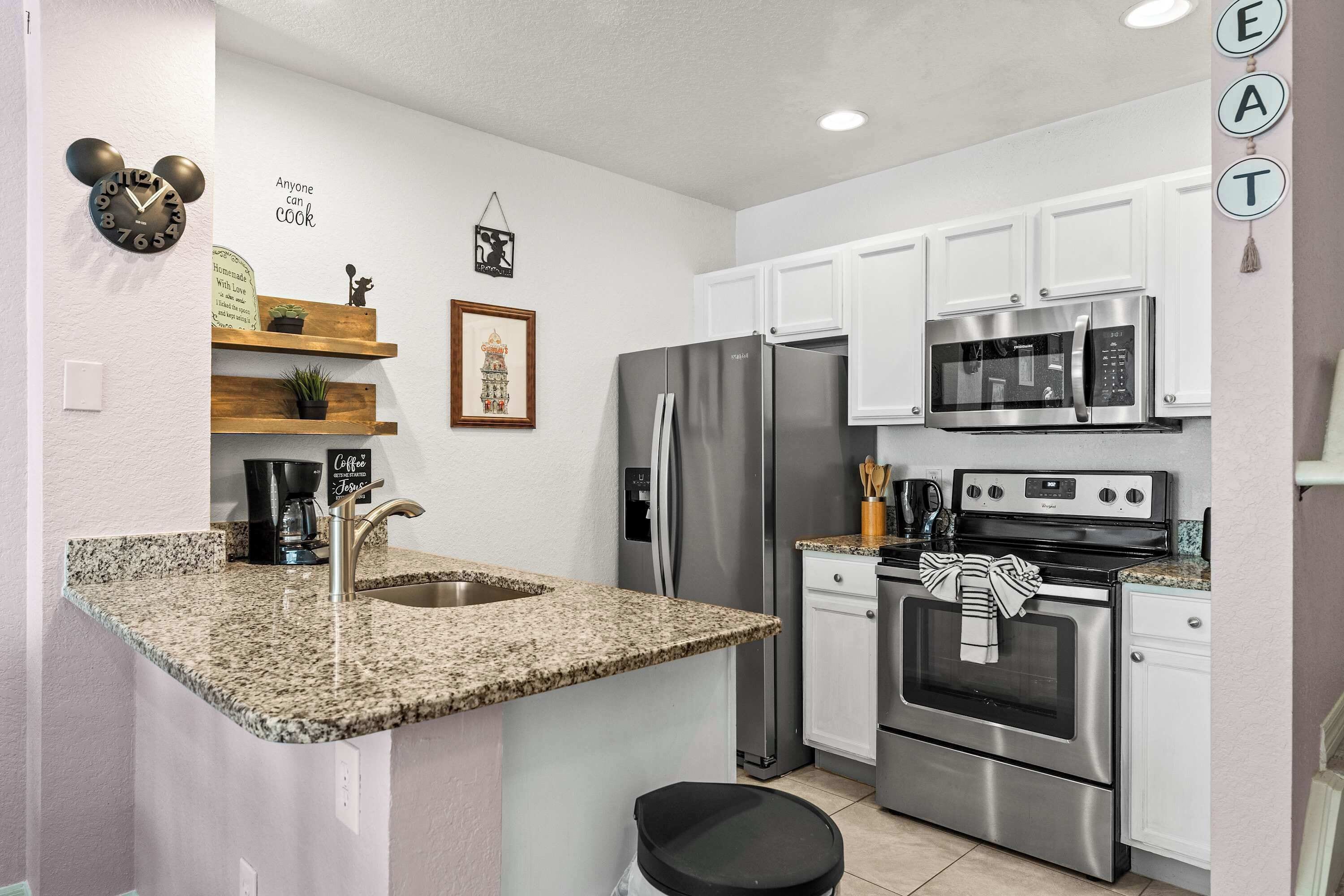 A modern kitchen with white cabinets, stainless steel appliances, a granite countertop, and a clock on the wall.