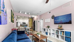 A living room with a blue sofa, a coffee table, a TV, and a bookshelf. - Enchanted At 7 Dwarfs Lane (Kissimmee)