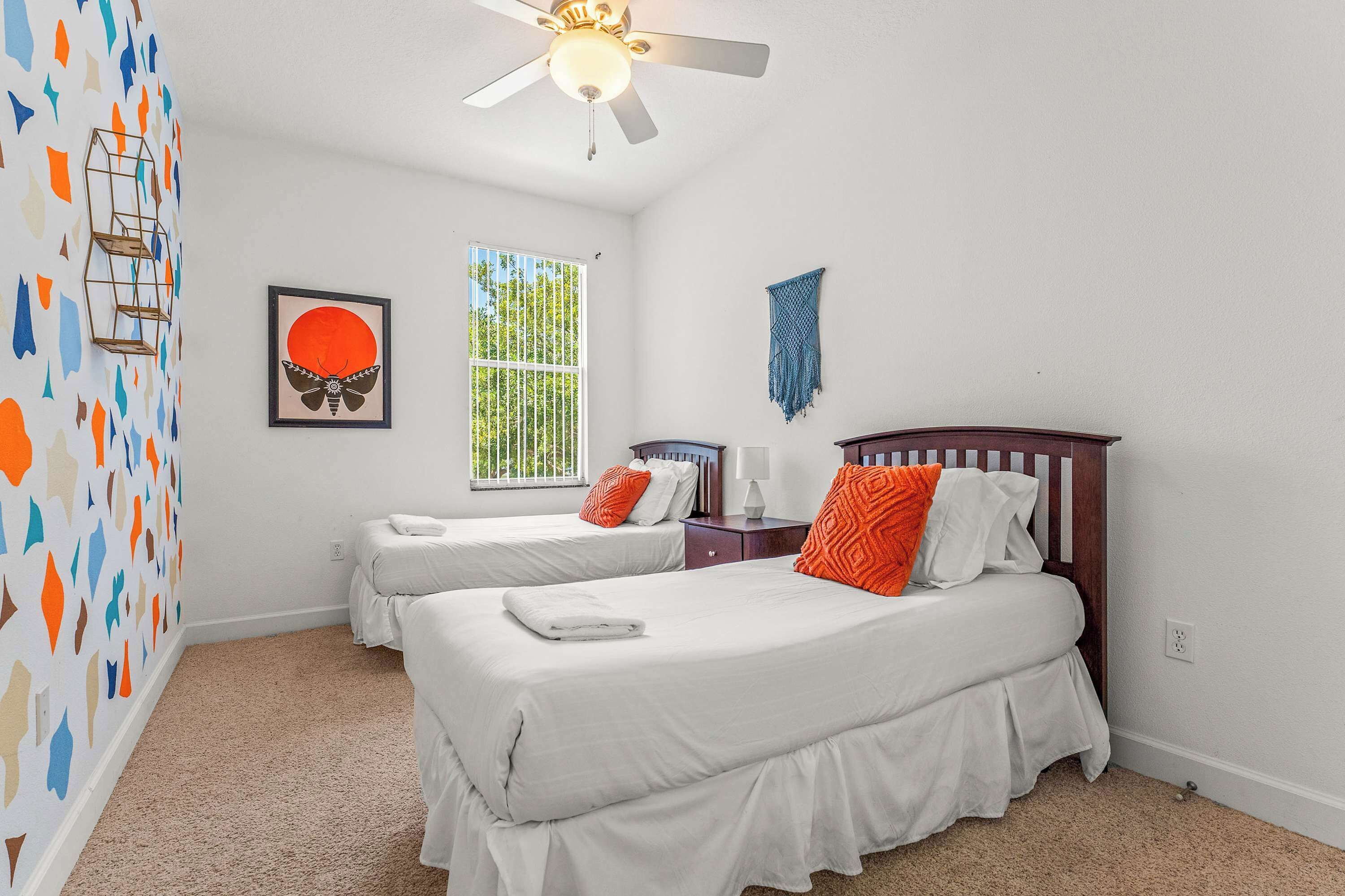 A bedroom with two beds, a ceiling fan, a window, and a wall decoration.