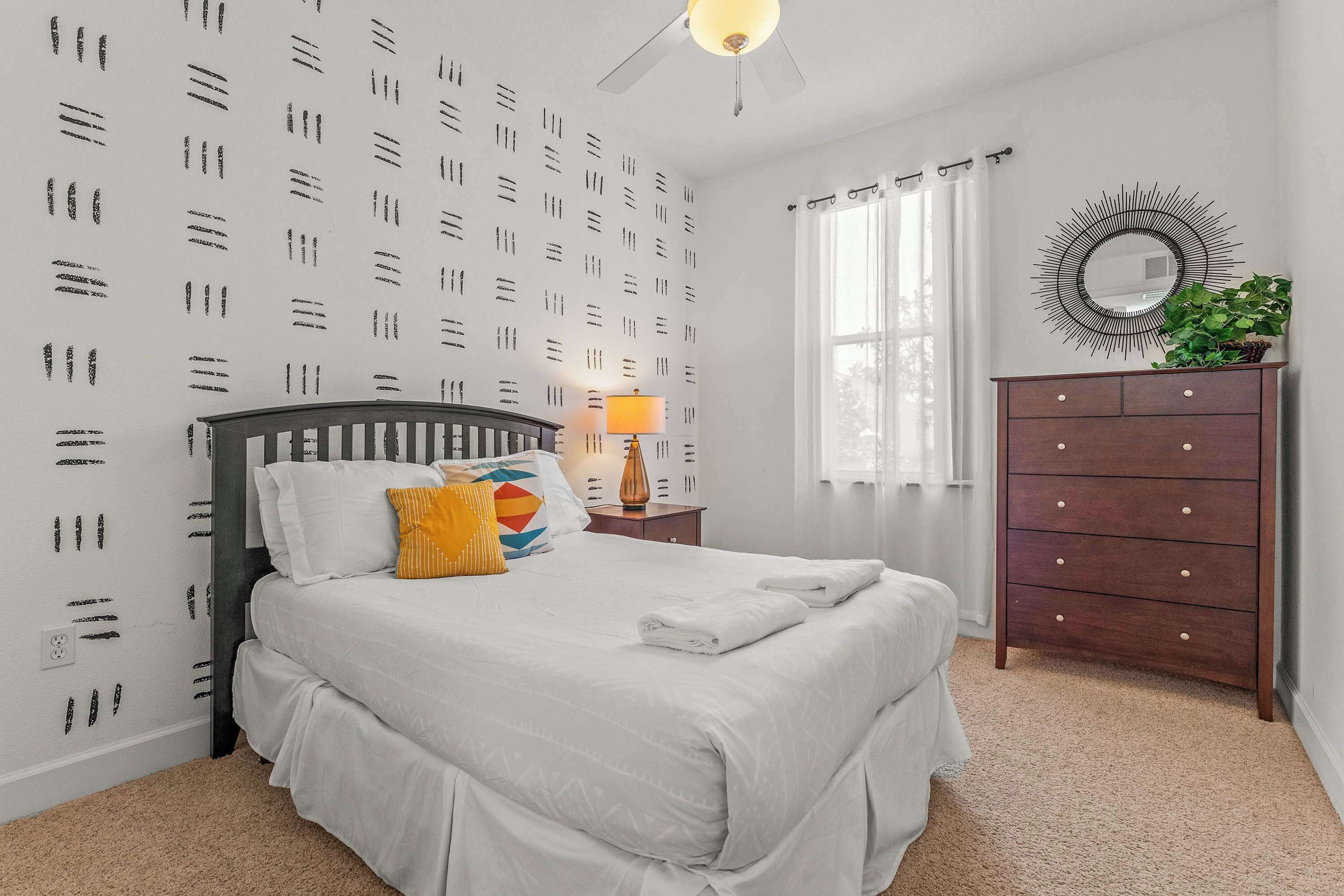 A bedroom with a bed, a dresser, a mirror, and a window with curtains.