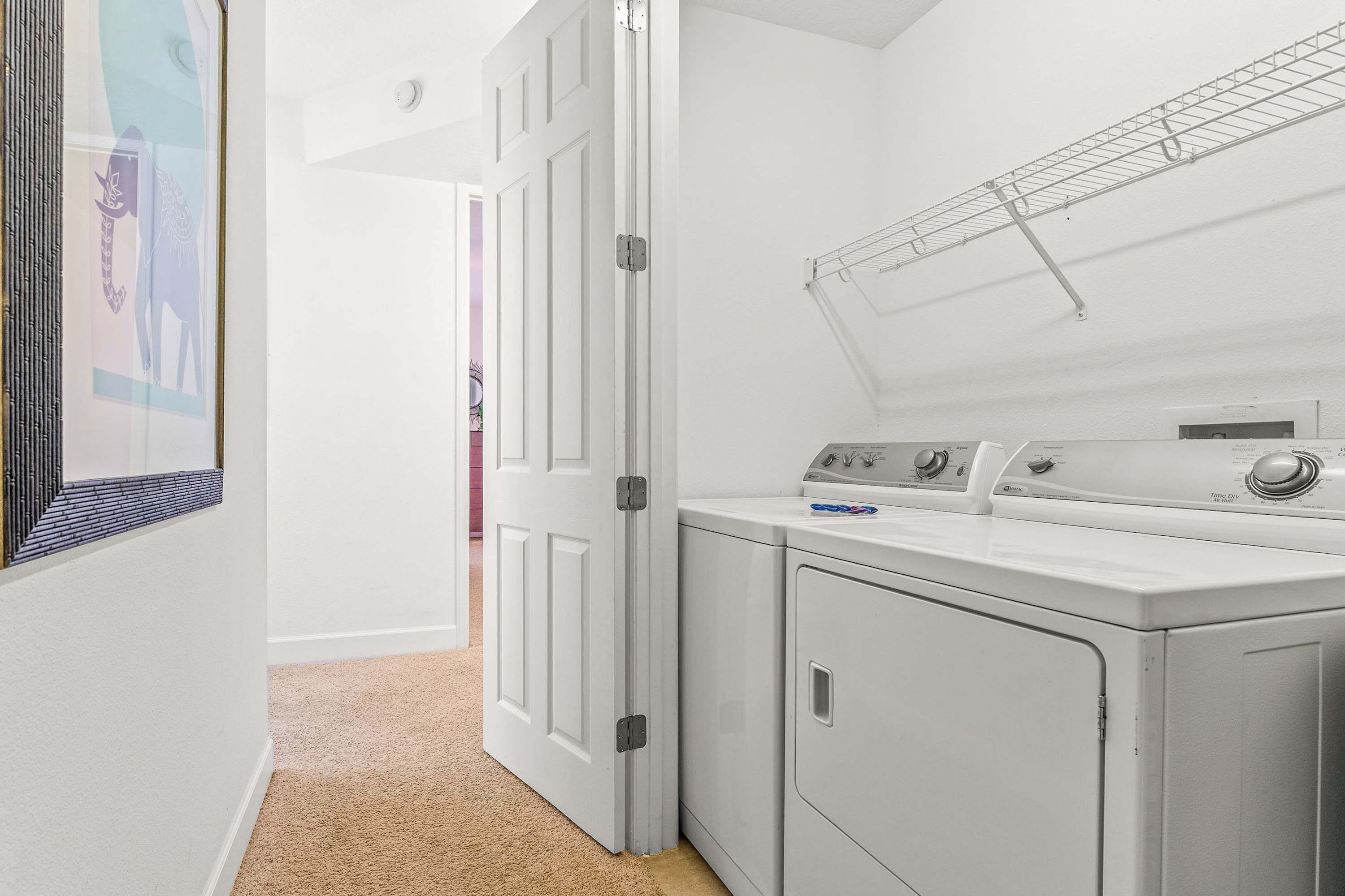 A laundry room with a washing machine and dryer, a door with a metal handle, and a wall-mounted drying rack.