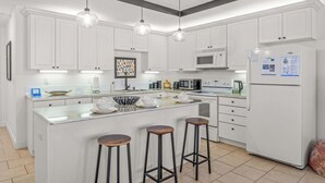 A modern kitchen with white cabinets, a central island with stools, a refrigerator, and a microwave. - Family Friendly Relax Villa (Kissimmee)