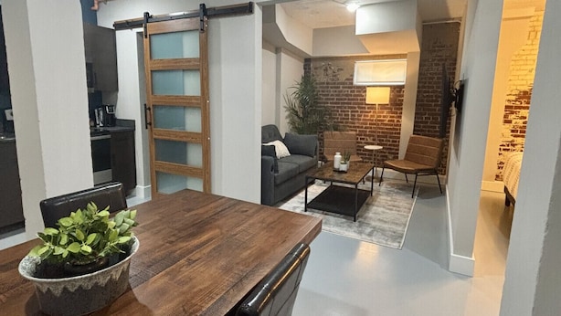 Een moderne eethoek met een houten tafel en stoelen, een plant in pot en een keuken op de achtergrond.