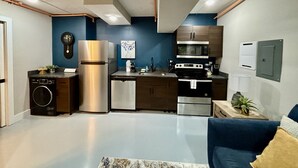 A compact kitchen with modern appliances, a washing machine, and a dining area with a blue sofa.