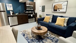 A modern living room with a blue sofa, a wooden coffee table, and a kitchen in the background.