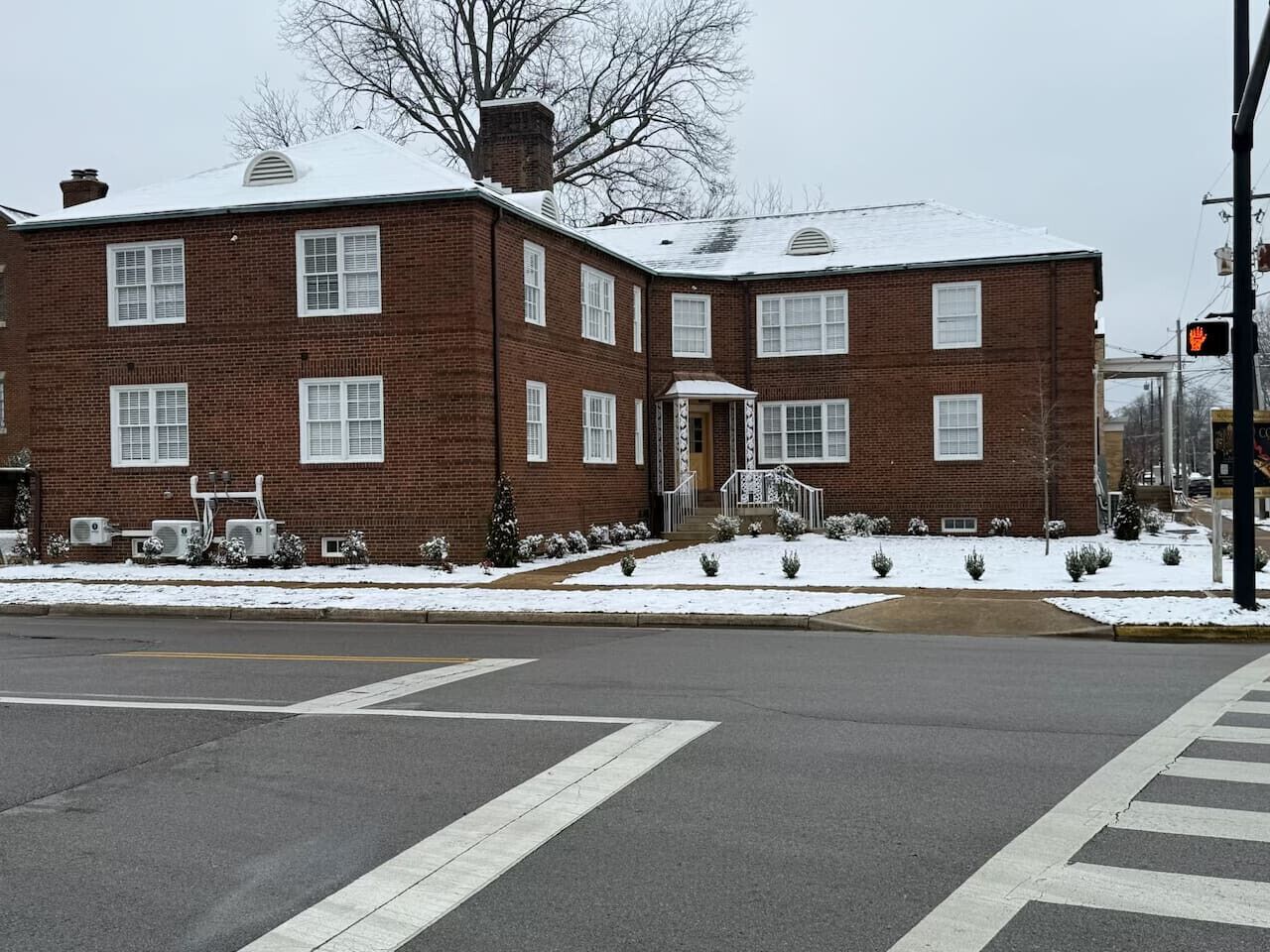 A brick building with a snow-covered roof and a crosswalk in front.