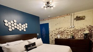 Ein Schlafzimmer mit Bett, einem Kopfteil, einer Wand mit sechseckartigen Verzierungen, einer Ziegelwand und einer Kommode mit Blumen.