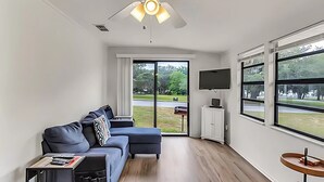 Una sala de estar moderna con un sofá seccional, un televisor de pantalla plana y ventanas amplias que dan a un paisaje exterior.