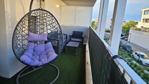 Un balcon avec un fauteuil suspendu, une petite table et un canapé.