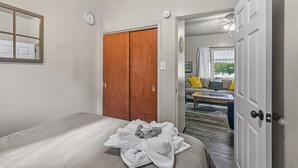 A bedroom with a bed, a wooden wardrobe, and a door leading to a living area with a sofa and a coffee table.