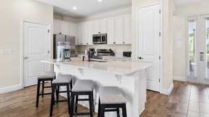 A kitchen with white cabinets, a central island with stools, and a stainless steel refrigerator. - Flamingo Paradise (Kissimmee)