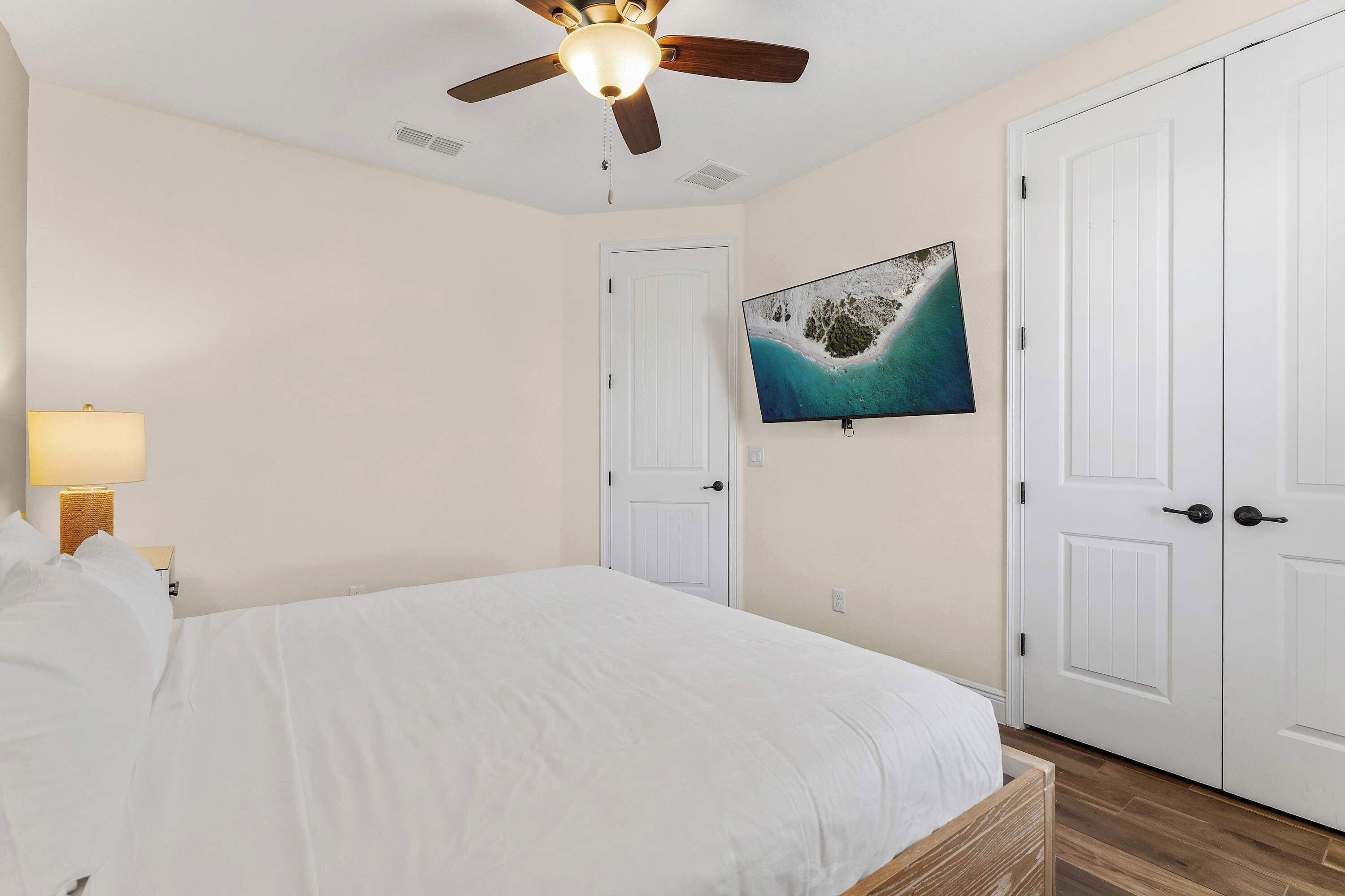 A bedroom with a bed, a ceiling fan, a TV, and a door.