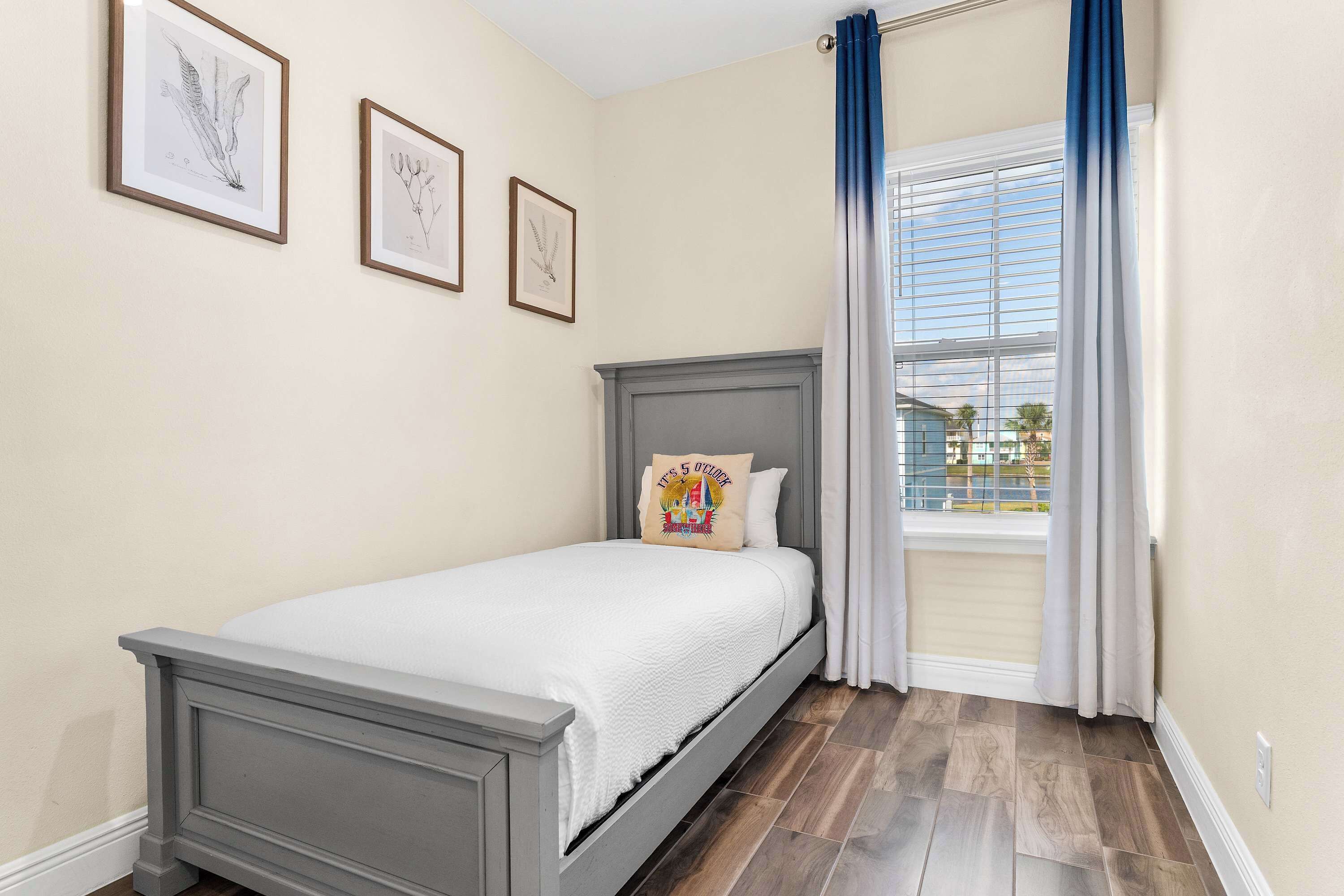 A bedroom with a bed, a window with curtains, and three framed botanical prints on the wall.
