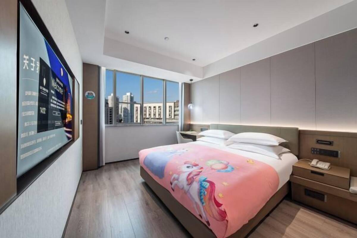 A hotel room with a large bed, a TV mounted on the wall, a city view, and a modern design.