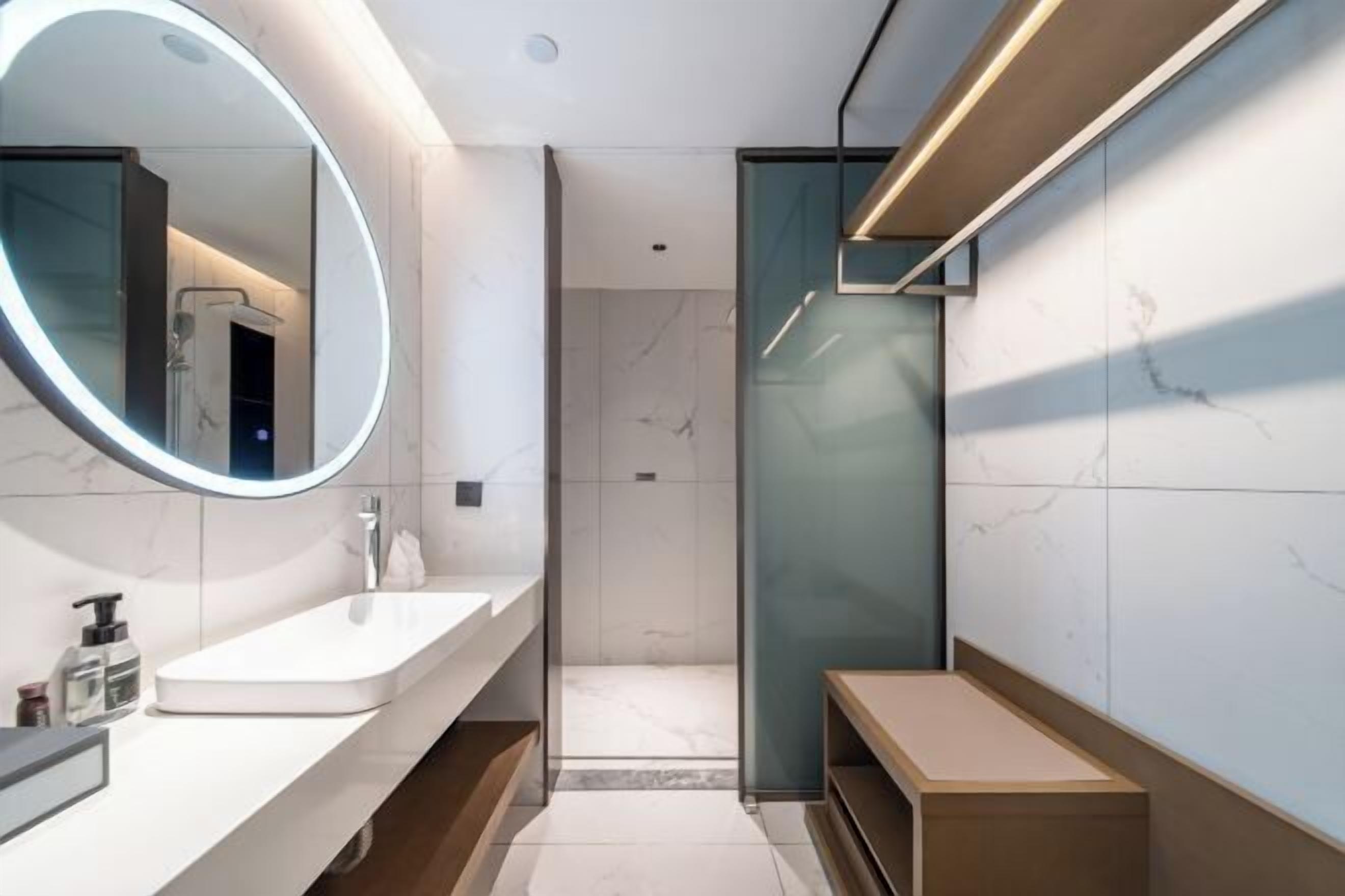 A modern bathroom with a large mirror, a sink, a shower, and a bench.