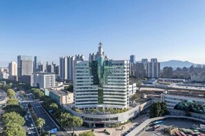 A modern high-rise hotel with a distinctive green facade, surrounded by a cityscape with other buildings and a clear sky. - Radow Wanrong Hotel (Wenzhou)