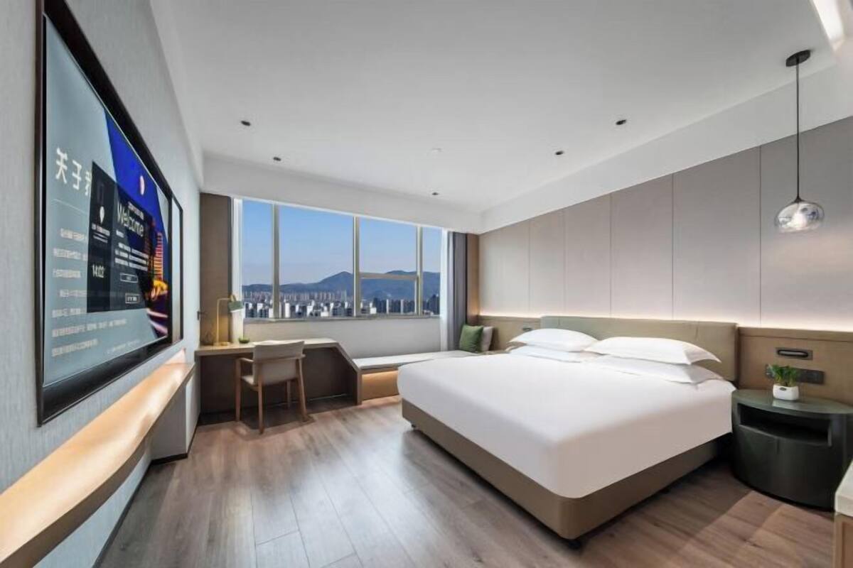 A modern hotel room with a large bed, a desk, and a city view.