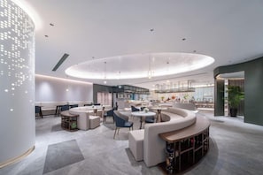 A modern interior with a circular seating area, a bar, and a reception desk. - Radow Wanrong Hotel (Wenzhou)