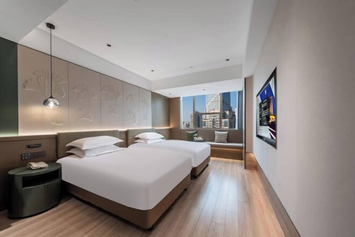 A modern hotel room with a large bed, bedside tables, a view of the city, and a large window.