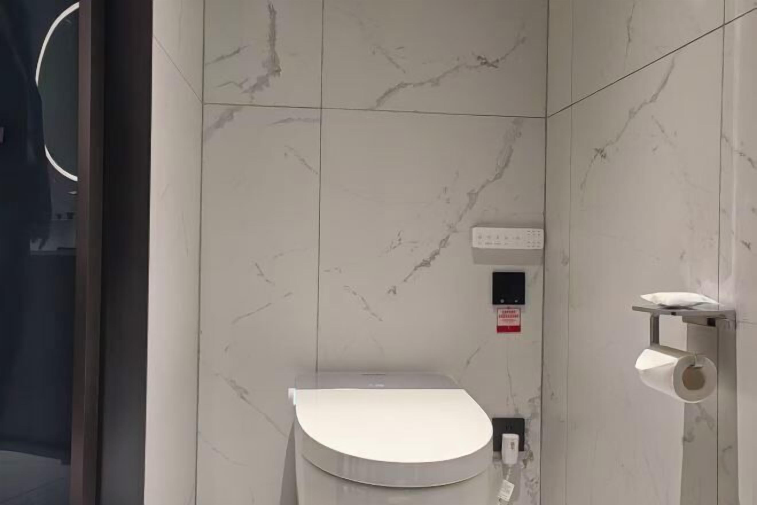 A modern bathroom with a marble wall, a toilet, a hand dryer, and a paper towel dispenser.