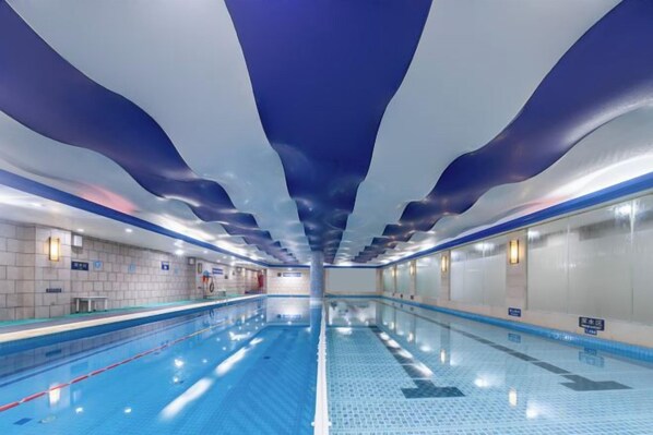 A swimming pool with clear lane markings, a tiled floor, and a ceiling with a wavy design. - Radow Wanrong Hotel (Wenzhou)