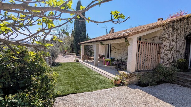 Un patio couvert avec des sièges d’extérieur, une pelouse bien entretenue et un chemin de gravier menant à l’entrée.