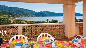 A balcony with a view of a lake and mountains, featuring a table with chairs and a floral tablecloth. - maison vue mer panoramique (Appietto)