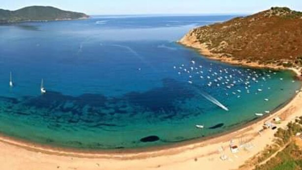 A coastal beach with clear waters, boats, and a hilly landscape in the background. - maison vue mer panoramique (Appietto)