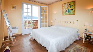A bedroom with a bed, a window, a door, a chair, a table, and a painting. - maison vue mer panoramique (Appietto)