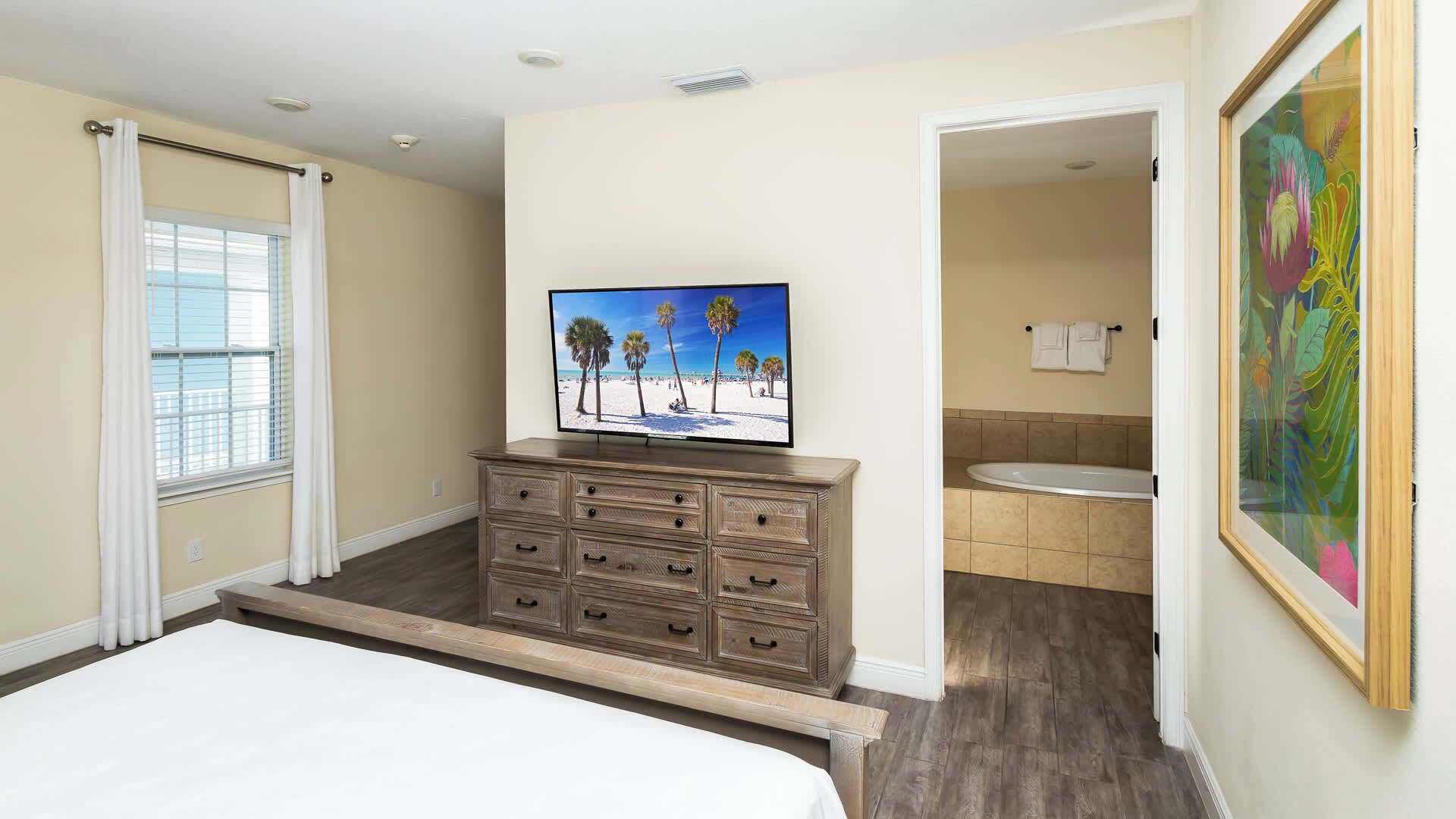 Une chambre avec un grand lit, une commode, un téléviseur fixé au mur et une salle de bain avec un lavabo et des toilettes.