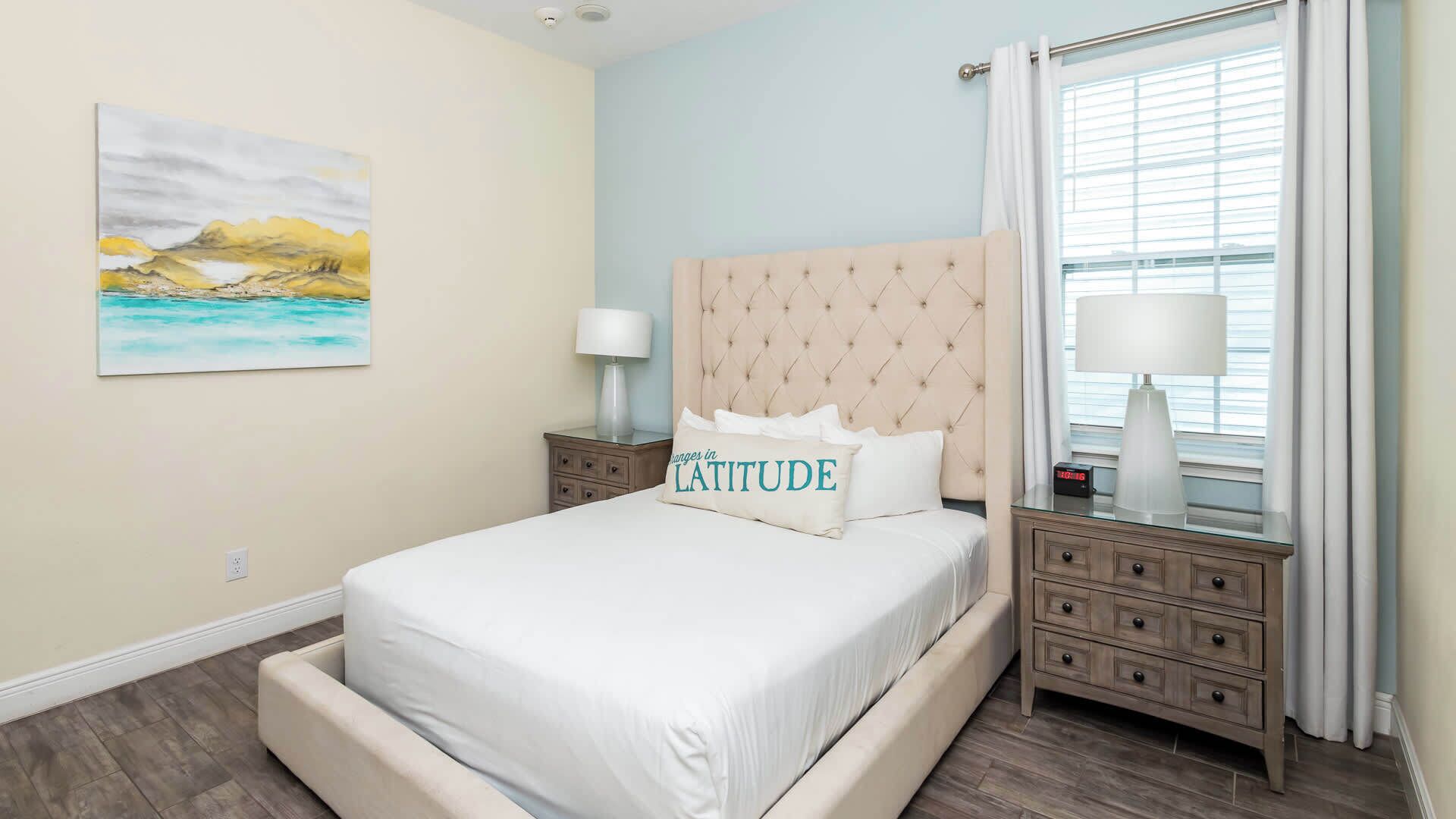 A hotel room with a bed, a nightstand, a lamp, a painting, and a window with curtains.